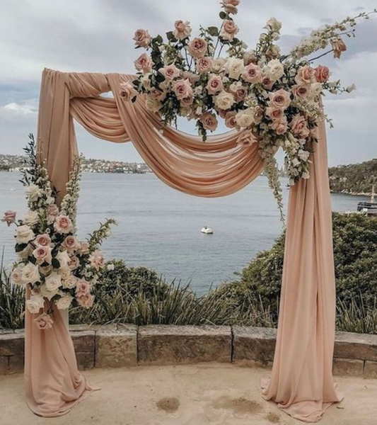 Arco floral para boda en la playa decorado con rosas y telas color nude.