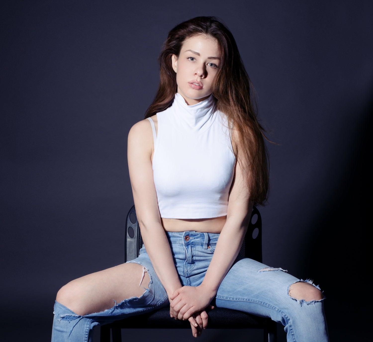Modelo sentada con top blanco y vaqueros rotos sobre fondo oscuro